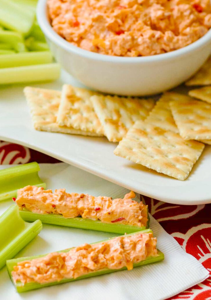 Homemade Pimento Cheese in a white bowl served with saltine crackers and celery sticks on a white platter.