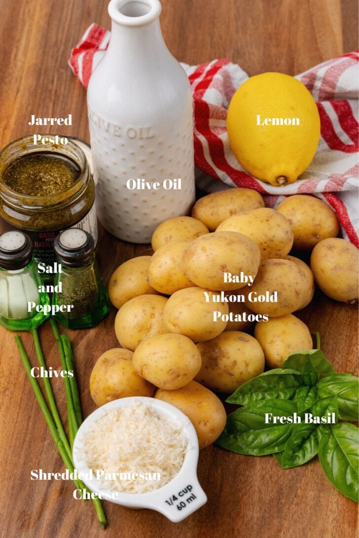 Yukon gold potatoes, jarred pesto, salt and pepper, lemon, shredded parmesan cheese, fresh basil, and olive oil on a wooden board.