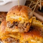 Roast Beef and Cheese Sliders stacked on a white plate on a wooden cutting board.