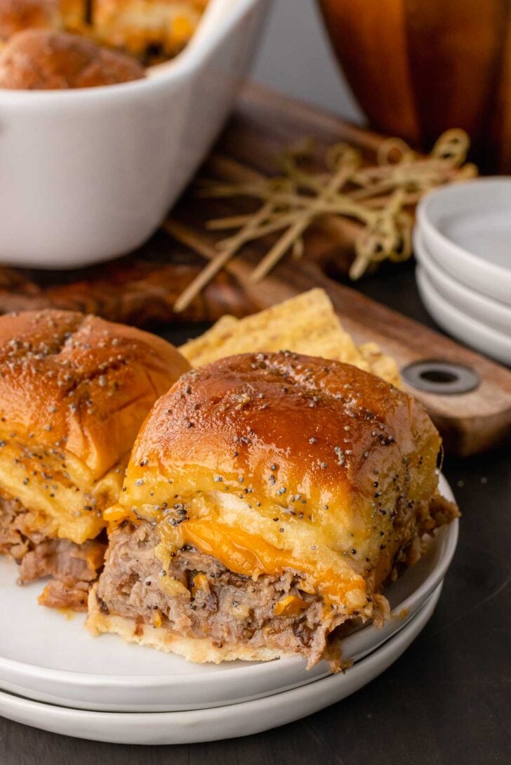 Two roast beef and cheese sliders on bread topped with poppy seeds on a white plate.