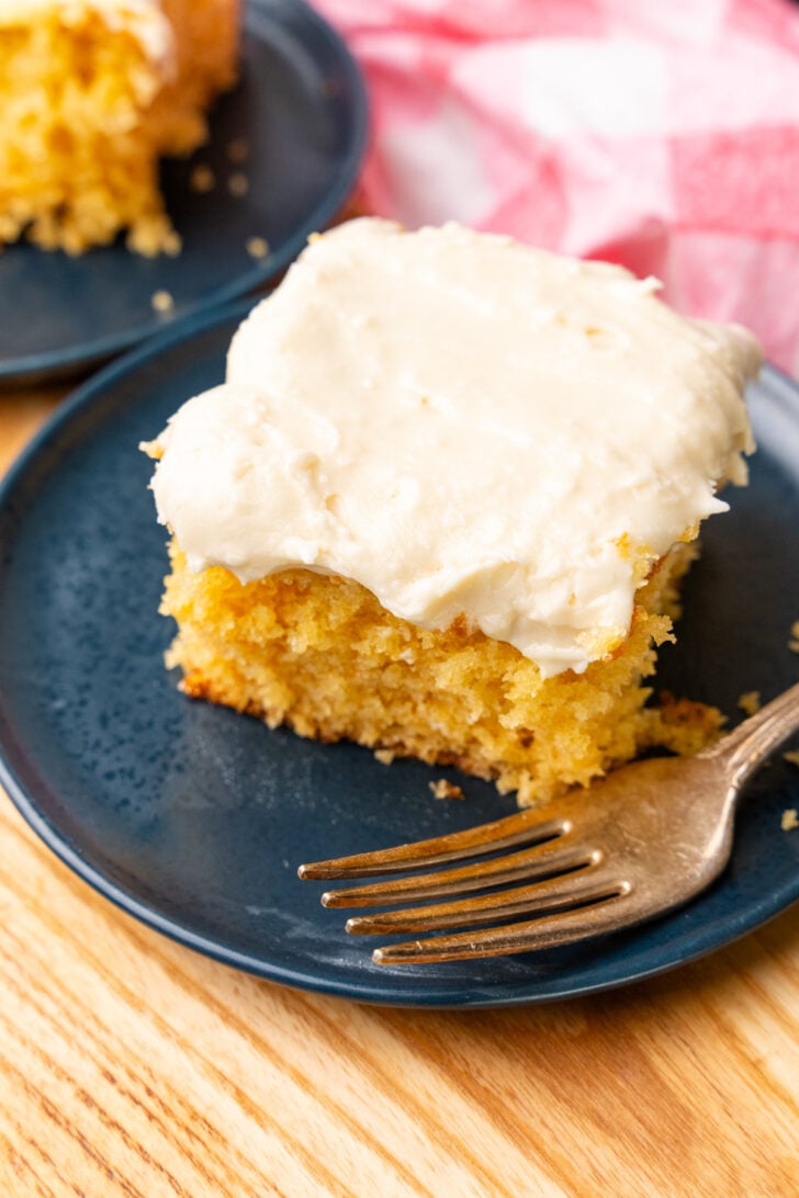 Slice of caramel snack cake with light, creamy caramel icing on a blue plate served with a silver fork.