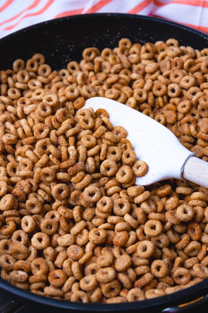 Cast iron skillet with buttered cinnamon fried cheerios scooped up with a white spatula.