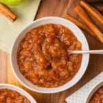 Homemade Crock Pot Applesauce in a white bowl served with a silver spoon on a board with green apples and cinnamon.