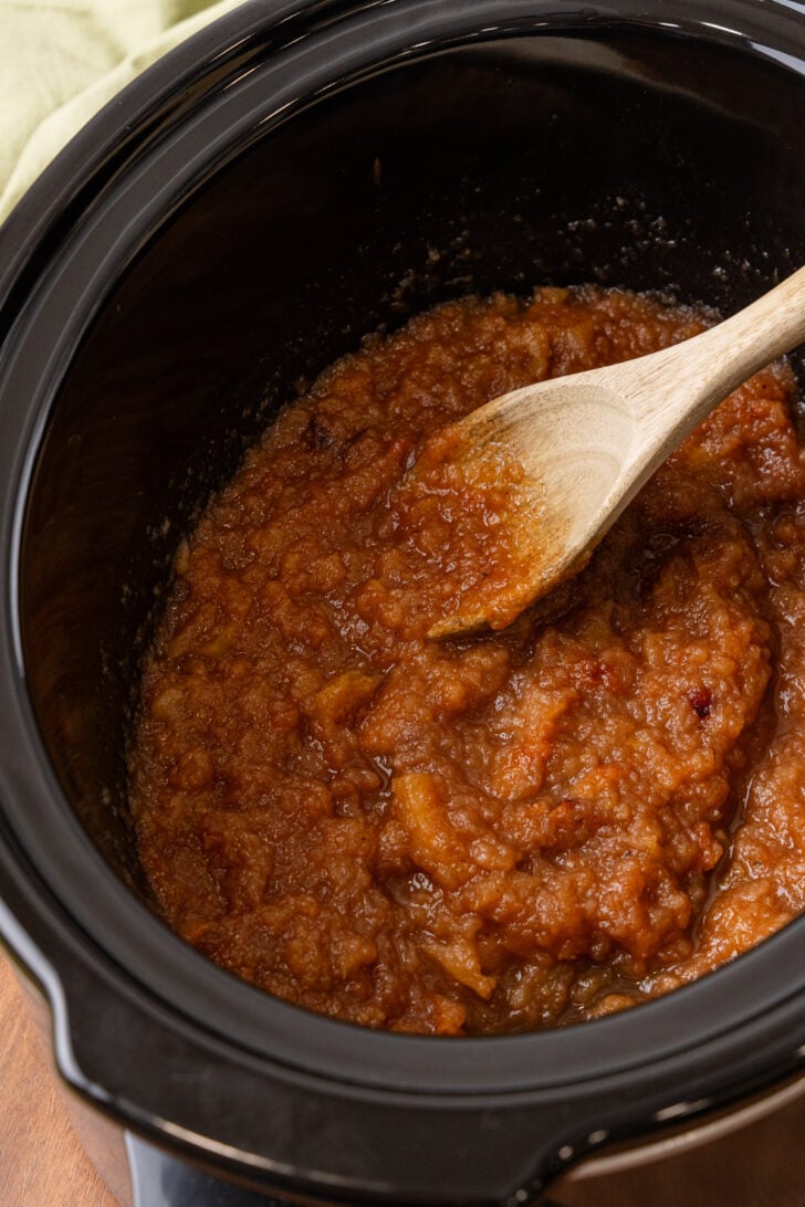 Homemade applesauce in a black crock pot served with a wooden spoon.