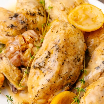Lemon chicken cooked in the crock pot on a white platter with garlic and a fresh thyme sprigs.