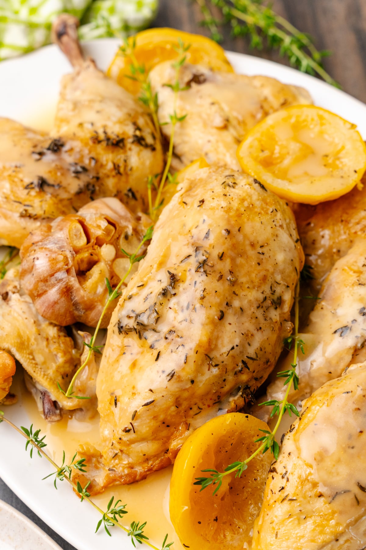 Lemon chicken cooked in the crock pot on a white platter with garlic and a fresh thyme sprigs.