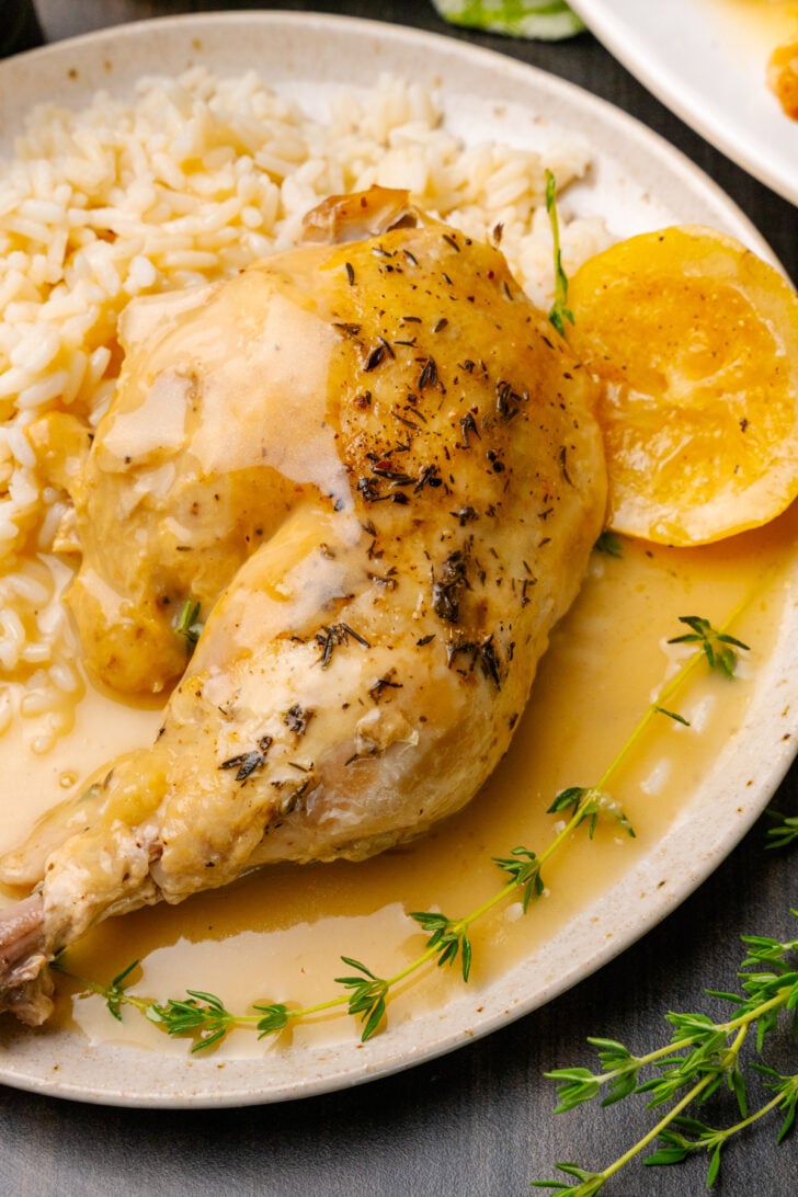 Lemon chicken cooked in the crock pot on a white platter with garlic and a fresh thyme sprigs.