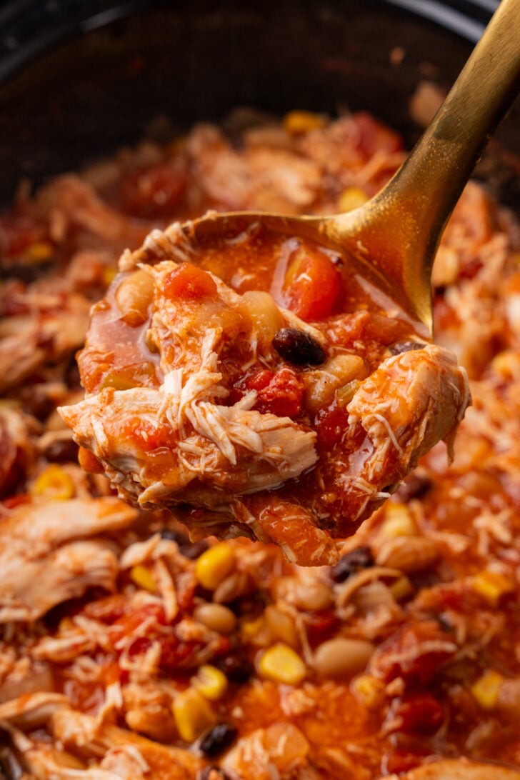 Gold ladle full of taco soup made with white meat chicken, corn, black beans, white beans.