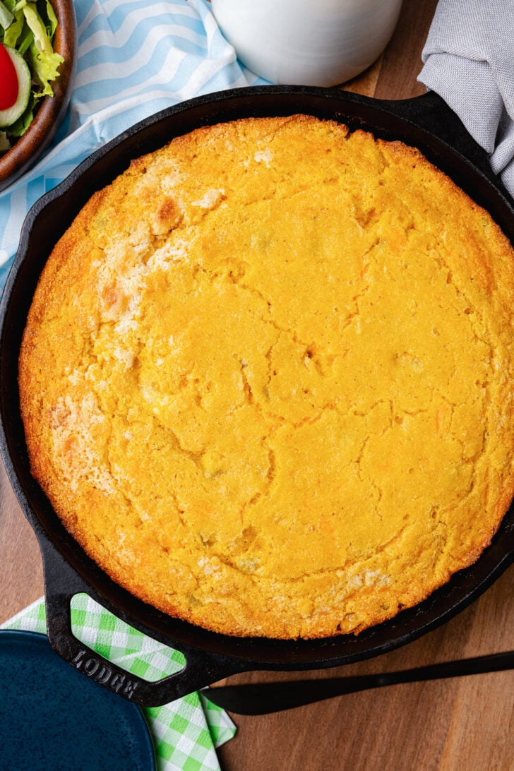 Black cast iron skillet with cooked green chile cheese corn bread on a wooden cutting board.