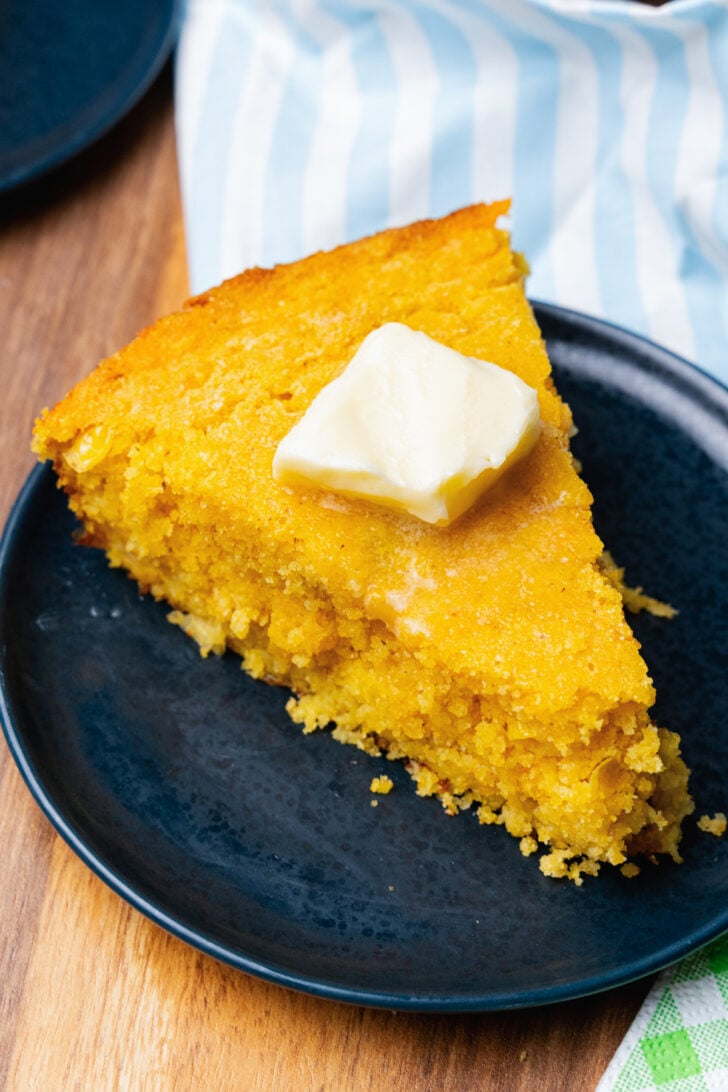 Slice of green chile cornbread with a pat of butter on a dark blue plate.