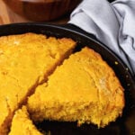 Green chile cheese cornbread in a black cast iron skillet sliced into pieces served with a green salad.