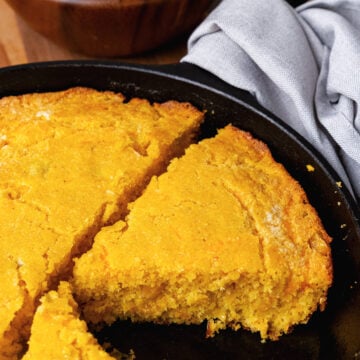 Green chile cheese cornbread in a black cast iron skillet sliced into pieces served with a green salad.