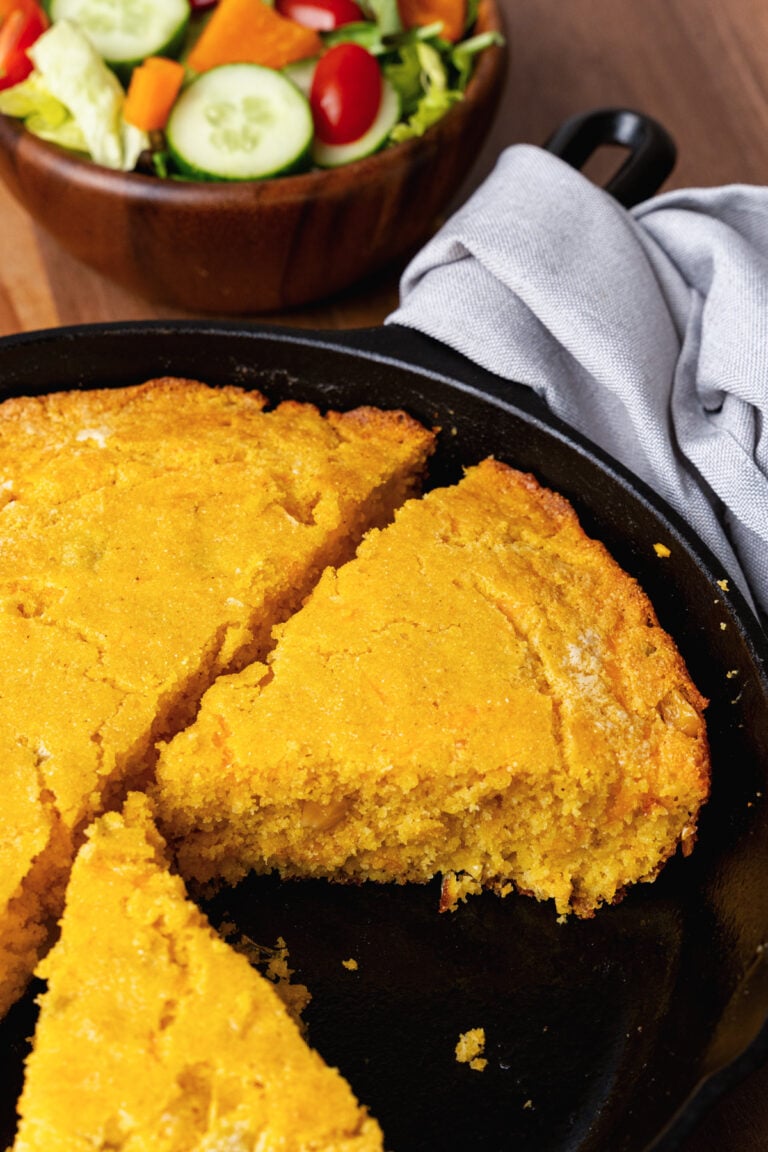 Green chile cheese cornbread in a black cast iron skillet sliced into pieces served with a green salad.