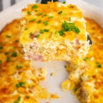 Square slice of ham and potato hashbrown casserole on a black spatula but from a white casserole dish.