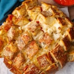 Round load of pepperoni pizza cheese bread with cut squares on parchment paper and a glass bowl of marinara sauce.