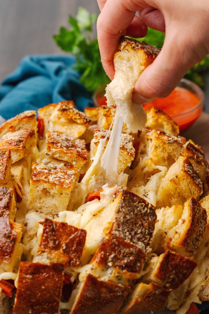 Hand pulling a piece of pepperoni pizza bread with a long string of cheese pull.