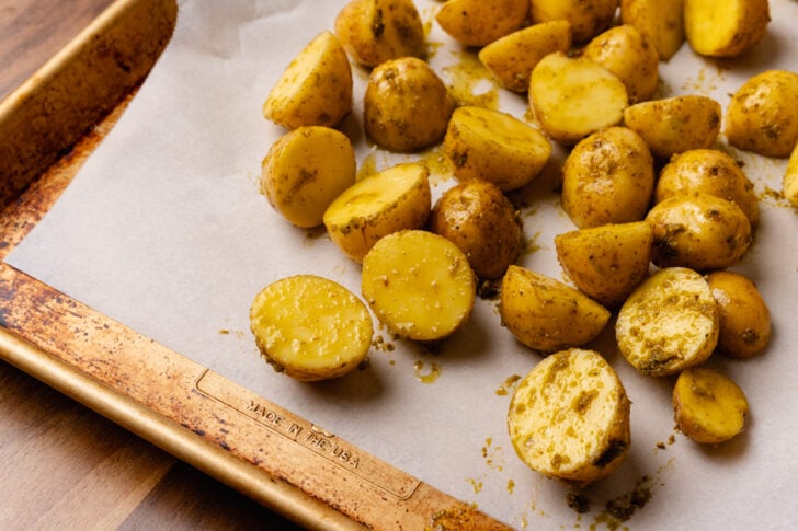 Raw yukon gold potatoes tossed in pesto and placed on a baking sheet lined with parchment.