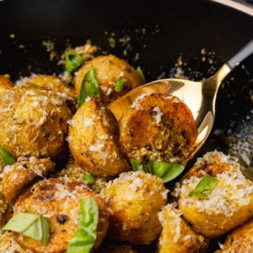 Black bowl with roasted pesto potato salad sprinkled with parmesan cheese and fresh basil.