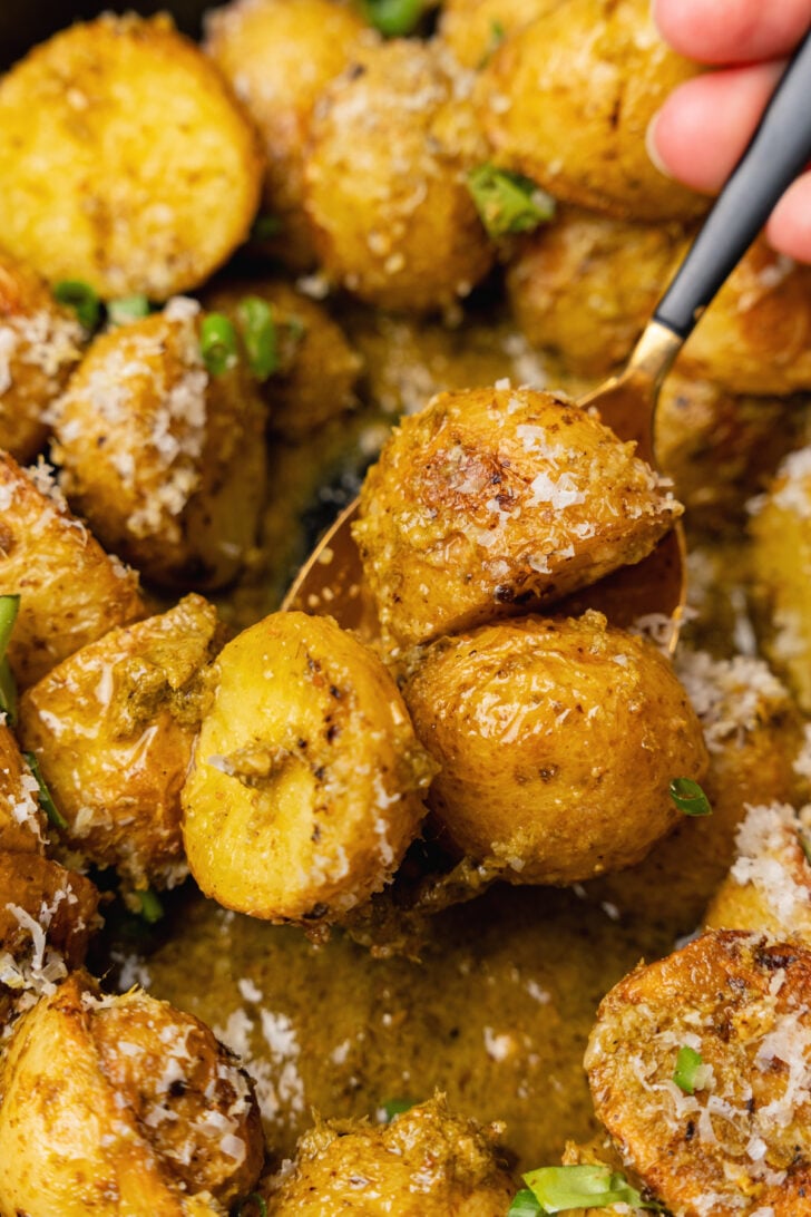 Spoon with roasted pesto potato salad sprinkled with fresh basil and grated Parmesan cheese.