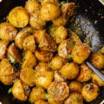 Black bowl with roasted pesto potato salad sprinkled with parmesan cheese and fresh basil.