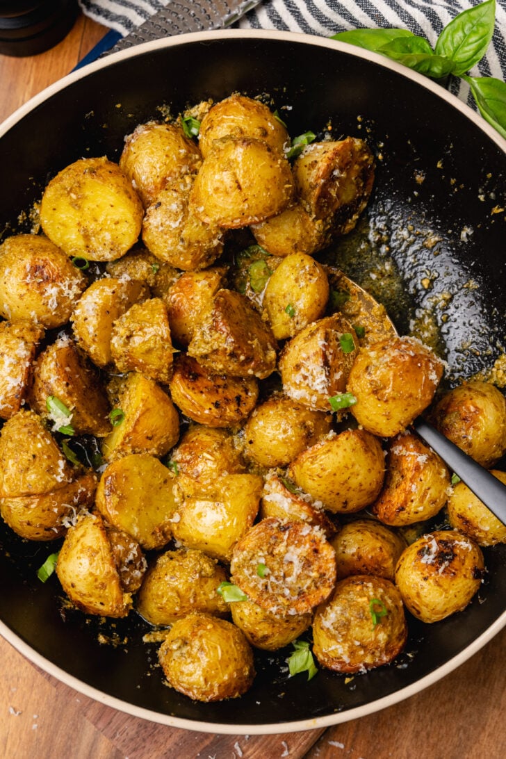 Black bowl with roasted pesto potato salad sprinkled with parmesan cheese and fresh basil.