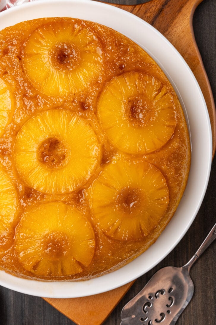 Pineapple upside down cake on a white plate with a silver serving utensil.