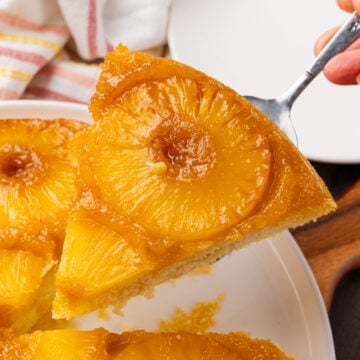 Slice of pineapple upside down cake served with a silver server from a white plate.