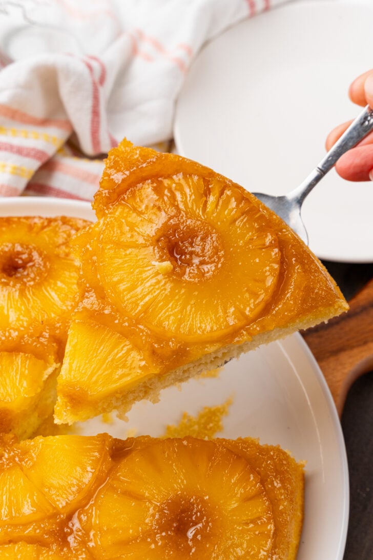 Slice of pineapple upside down cake served with a silver server from a white plate.