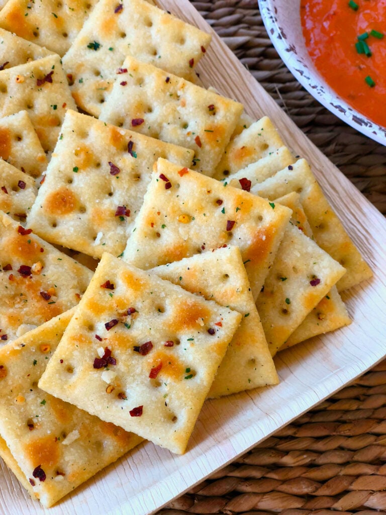 Saltine crackers with red pepper flakes and ranch dressing served on a white plate alongside tomato soup.
