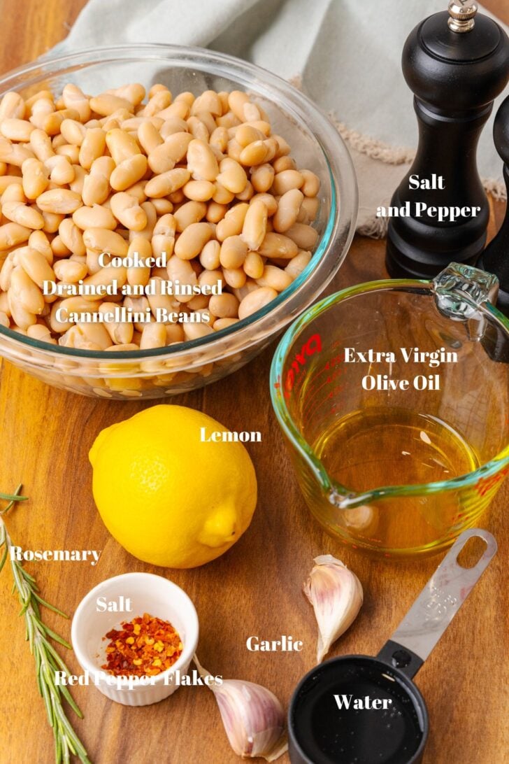 Cooked white beans, salt and pepper, olive oil, a whole lemon, fresh rosemary, garlic, water, salt and red pepper flakes o a wooden board for white bean dip.