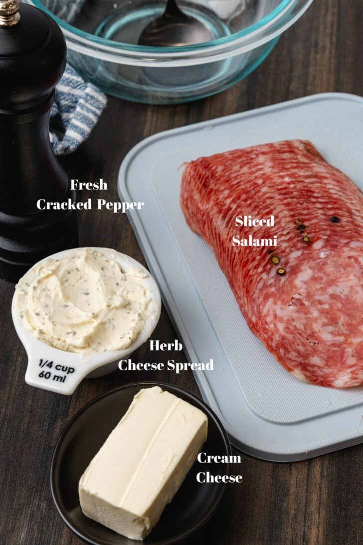 Salami, cream cheese, herb cheese, and fresh cracked pepper on a wooden cutting board.