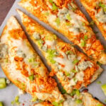 Flatbread topped with buffalo chicken, blue cheese, celery and mozzarella then baked, cut into triangles on a wooden cutting board topped with parchment paper.