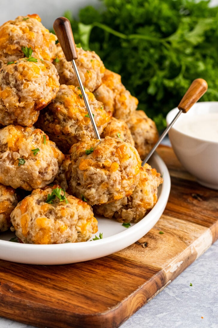 Cream cheese sausage balls on a white plate with serving skewers on a wooden board.