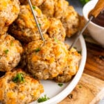 Cream cheese sausage balls served with metal skewers on a white plate with fresh parsley resting on a wooden serving board.