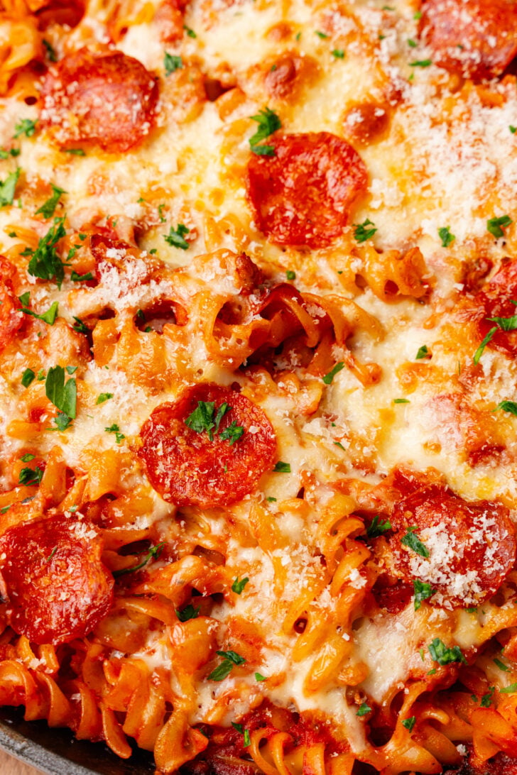 Baked pizza pasta casserole with melted mozzarella cheese and slices of pepperoni then topped with chopped green parsley.