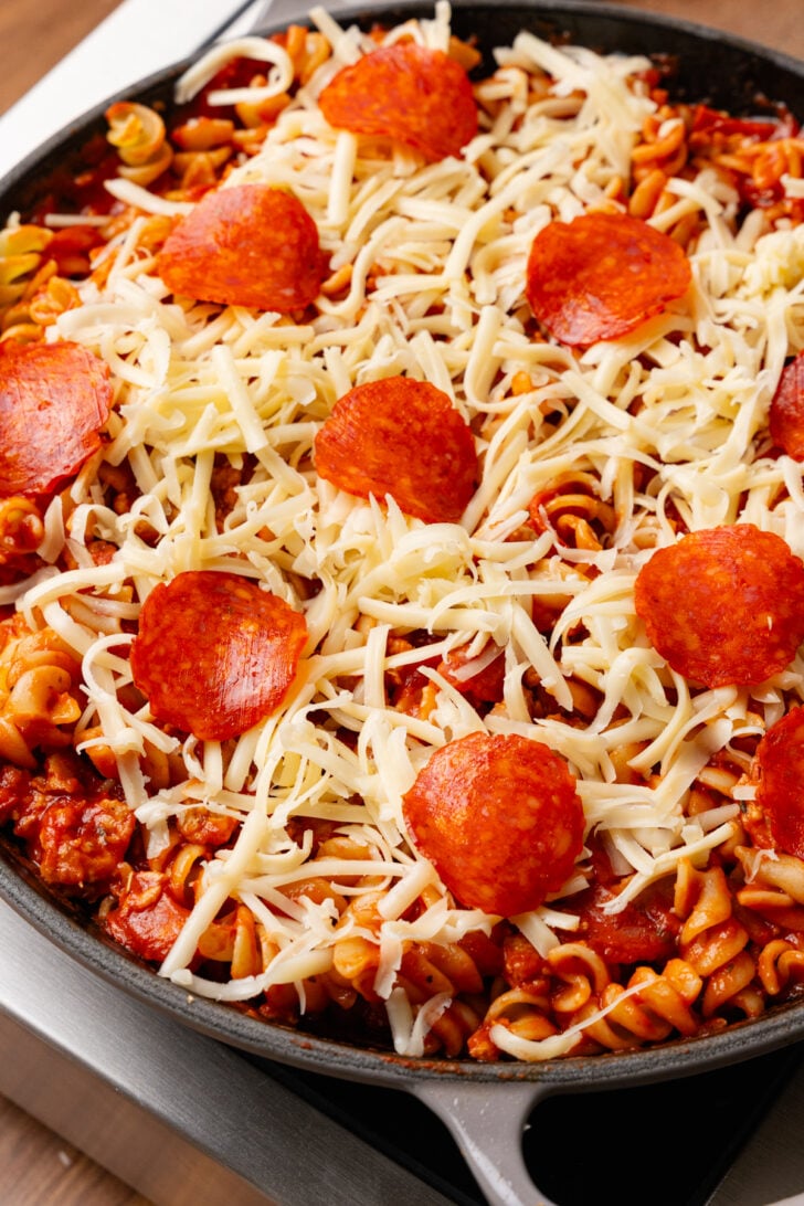 Gray skillet with pizza pasta bake topped with shredded mozzarella cheese and slices of pepperoni.