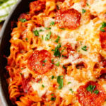 Baked pizza pasta casserole with melted mozzarella cheese and slices of pepperoni then topped with chopped green parsley.