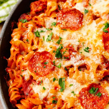Baked pizza pasta casserole with melted mozzarella cheese and slices of pepperoni then topped with chopped green parsley.