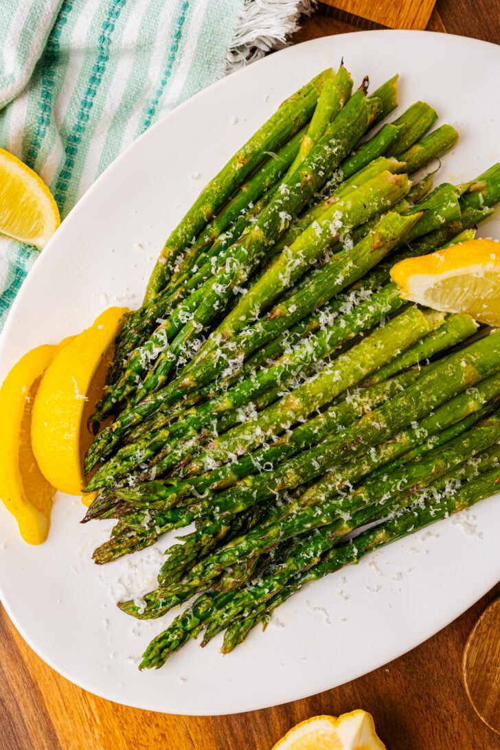 Roasted asparagus topped with grated Parmesan cheese and lemon on a white plated.