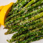 Roasted asparagus topped with grated Parmesan cheese and lemon on a white plated.