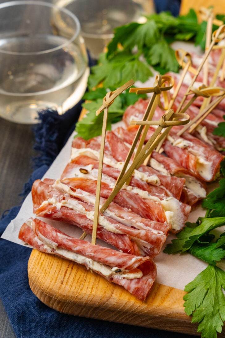 Wooden cutting board with cream cheese filled salami slices with a wooden pick.