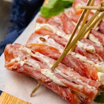 Wooden cutting board with cream cheese filled salami slices with a wooden pick.