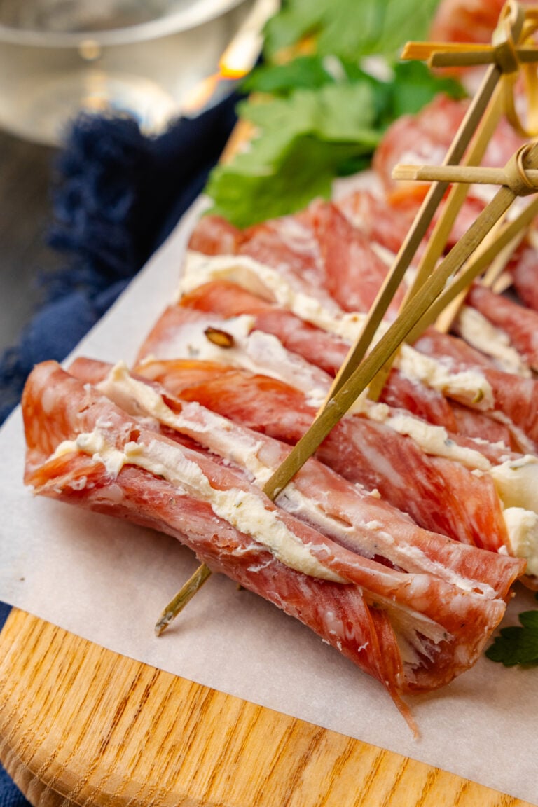 Wooden cutting board with cream cheese filled salami slices with a wooden pick.