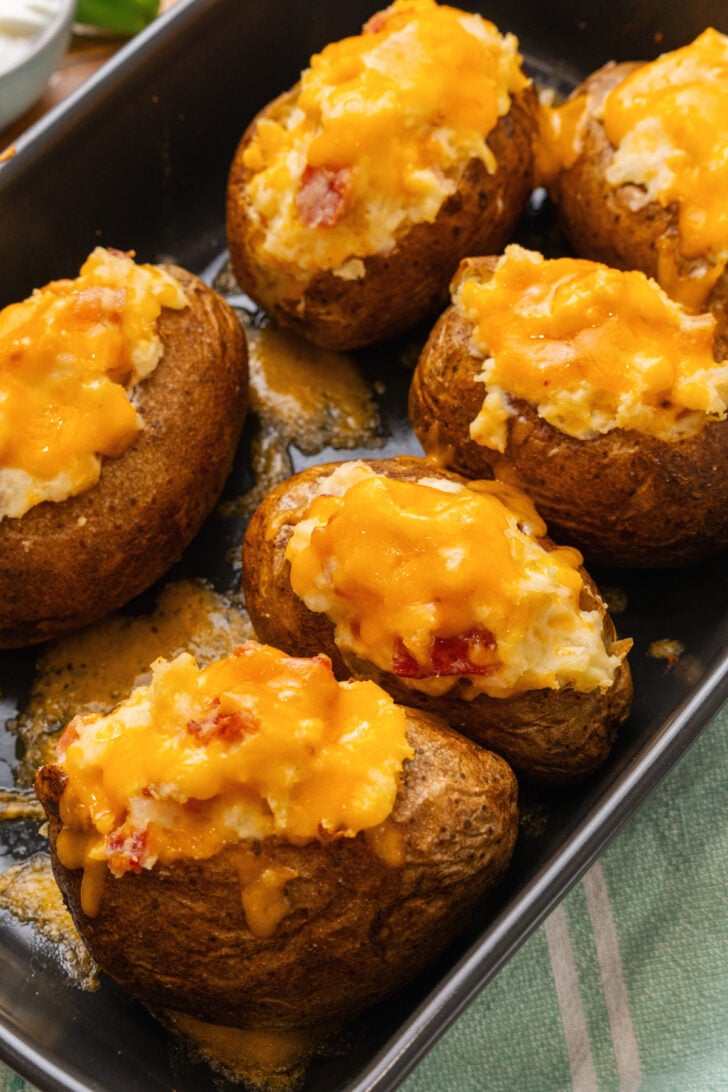 Stuffed baked potatoes topped with shredded cheddar cheese in a metal baking pan.