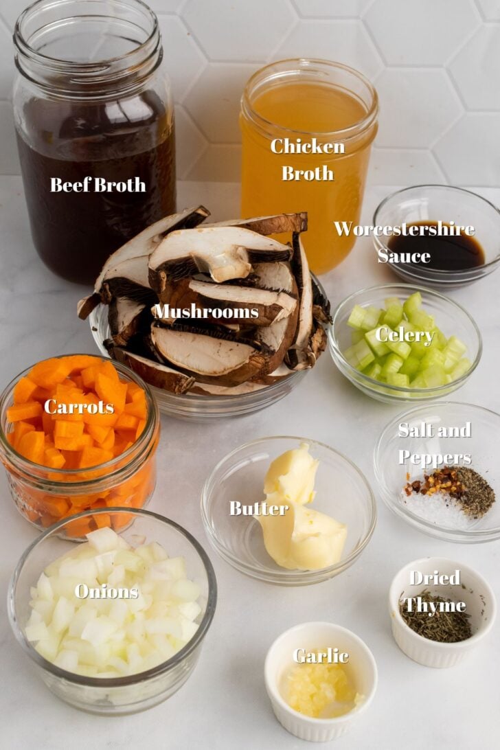 Beef broth, chicken broth, mushrooms, carrots, worcestershire sauce, celery, butter, onions, salt, pepper, thyme and garlic in glass bowls on a kitchen counter.
