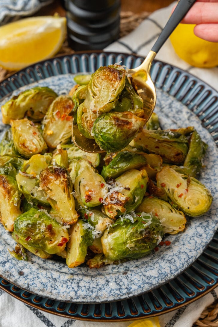 Gold metal spoon serving roasted brussels sprouts from a blue plate.