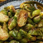 Roasted brussels sprouts on a blue plate with a gold metal spoon.