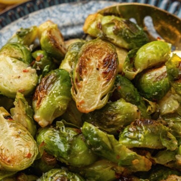 Roasted brussels sprouts on a blue plate with a gold metal spoon.