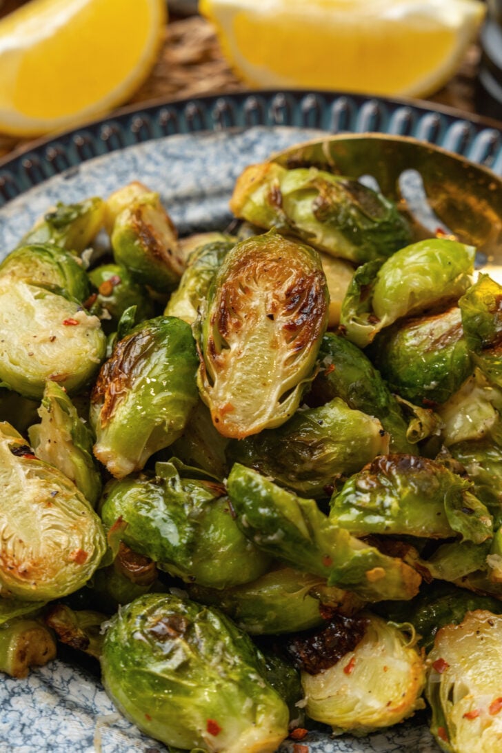 Roasted brussels sprouts on a blue plate with a gold metal spoon.