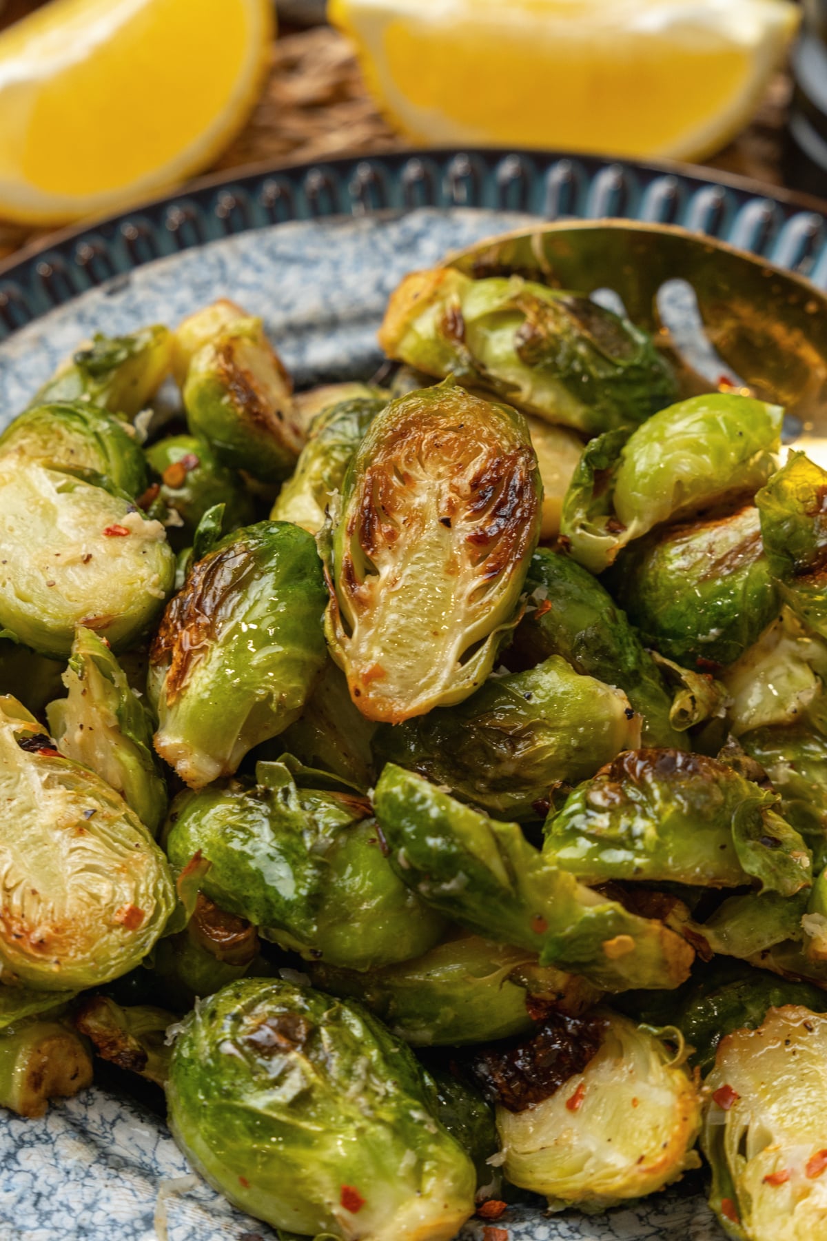 Roasted brussels sprouts on a blue plate with a gold metal spoon.